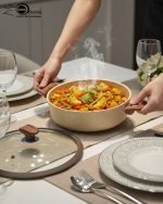 Falez 9-piece beige granite non-stick cookware set arranged on a kitchen surface, featuring three deep pots, one shallow casserole, and one fry pan with wood-effect handles and glass lids, made in Turkey.