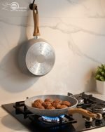 Falez 9-piece grey granite non-stick cookware set displaying a frying pan, shallow casserole, and deep pots with glass lids and wooden-style handles on a kitchen countertop.