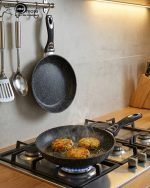 Stack of One More black granite non-stick cooking pots in four sizes (22cm, 24cm, 26cm, and 28cm) with ergonomic handles, displaying a premium speckled texture.