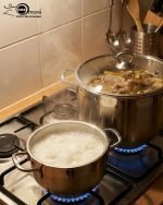 Stacked collection of Falez stainless steel cooking pots in seven sizes ranging from 18cm to 30cm, featuring glass lids and a polished silver finish, displayed on a wooden table for the One More kitchenware brand.
