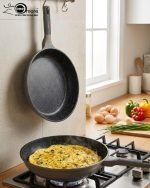 UCC LIFE 9-piece non-stick granite cookware set arranged on a wooden kitchen counter, featuring a frying pan, shallow casserole, and three pots with glass lids in a speckled grey finish.
