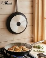 Falez 9-piece black granite non-stick cookware set including fry pan, shallow casserole, and three pots with glass lids and stainless steel handles, arranged on a wooden table.