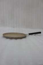 Falez non-stick granite crepe pan in beige speckled finish, shown cooking a golden-brown crepe on a gas stove with a wooden spreader. Option 2: Person flipping a crepe in a Falez granite coated pan, demonstrating non-stick surface and low-oil cooking capabilities.