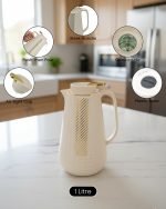 1 Litre vacuum flask thermos jug featuring a textured geometric design and gold accent strip. Shown in Off-White, Grey, and Black colors on a marble kitchen counter with callouts highlighting the glass interior, sleek handle, and air-tight cap.