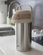 3-Liter Stainless Steel Airpot Thermos Flask with pump action dispenser and glass liner, displayed on a kitchen counter in Blue, Brown, and Green color options. Features callouts for rotating base, air-tight cap, and sleek handle.
