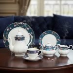An elegant 24-piece white ceramic tea set with a teal floral border and pink cherry blossoms, featuring steaming tea on a dark wooden table in a cinematic lighting setting.