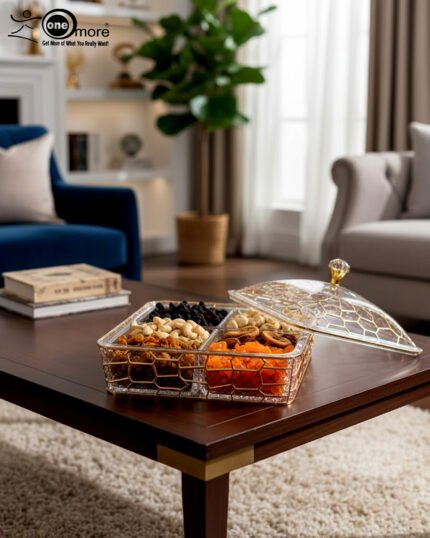 A luxury 4-compartment clear acrylic dry fruit box with a gold honeycomb pattern, filled with assorted nuts and dried apricots, displayed on a dark wooden coffee table in a modern living room.