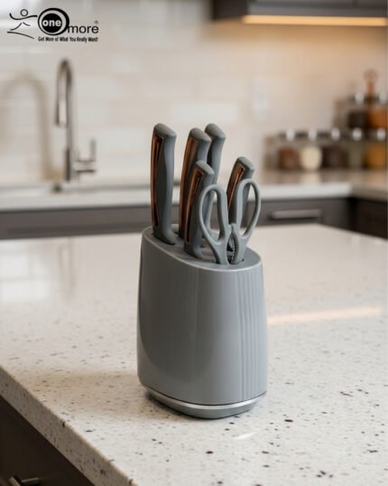 A modern 6-piece kitchen knife set by OneMore featuring grey ergonomic handles with copper accents, displayed both inside a sleek grey storage block on a granite countertop and laid out on a white surface to show the stainless steel blades and matching kitchen shears.