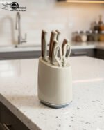A 6-piece kitchen knife set featuring cream-colored ergonomic handles with rose gold accents, displayed both inside a matching compact storage block on a granite countertop and laid out on a white surface to show the different stainless steel blades and kitchen shears.