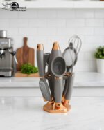 A professional 7-piece kitchen gadget set with rose gold and black ergonomic handles, featuring a pizza cutter, whisk, and grater, organized on a sleek black rotating stand.
