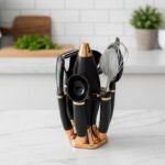 A premium 7-piece kitchen gadget set with rose gold and black handles, featuring a pizza cutter, whisk, and grater, organized on a sleek black rotating stand.