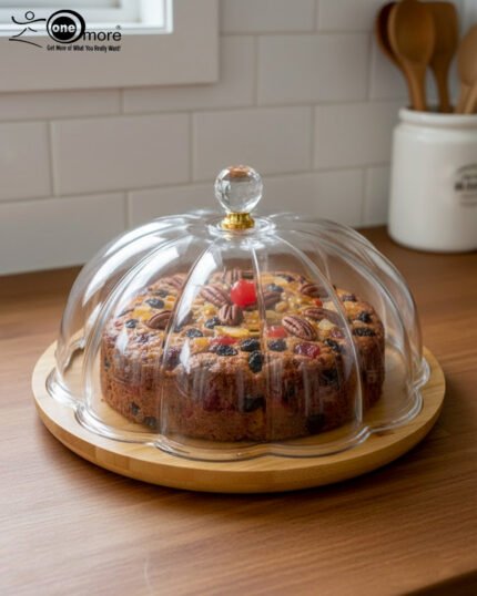 Two round cake stands of different sizes on a white kitchen counter, featuring natural wooden bamboo bases and clear ribbed acrylic dome covers with decorative crystal knobs, containing fruit cakes.