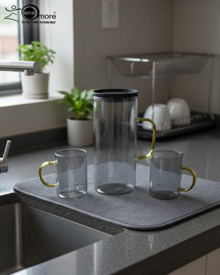 A person carrying a black serving tray with a modern smoke-grey glass water pitcher and six matching mugs with amber handles, filled with ice water in a bright, minimalist living room.