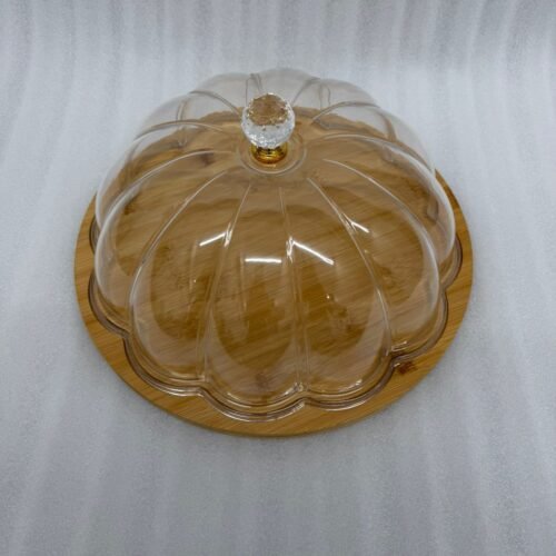 Two round cake stands of different sizes on a white kitchen counter, featuring natural wooden bamboo bases and clear ribbed acrylic dome covers with decorative crystal knobs, containing fruit cakes.