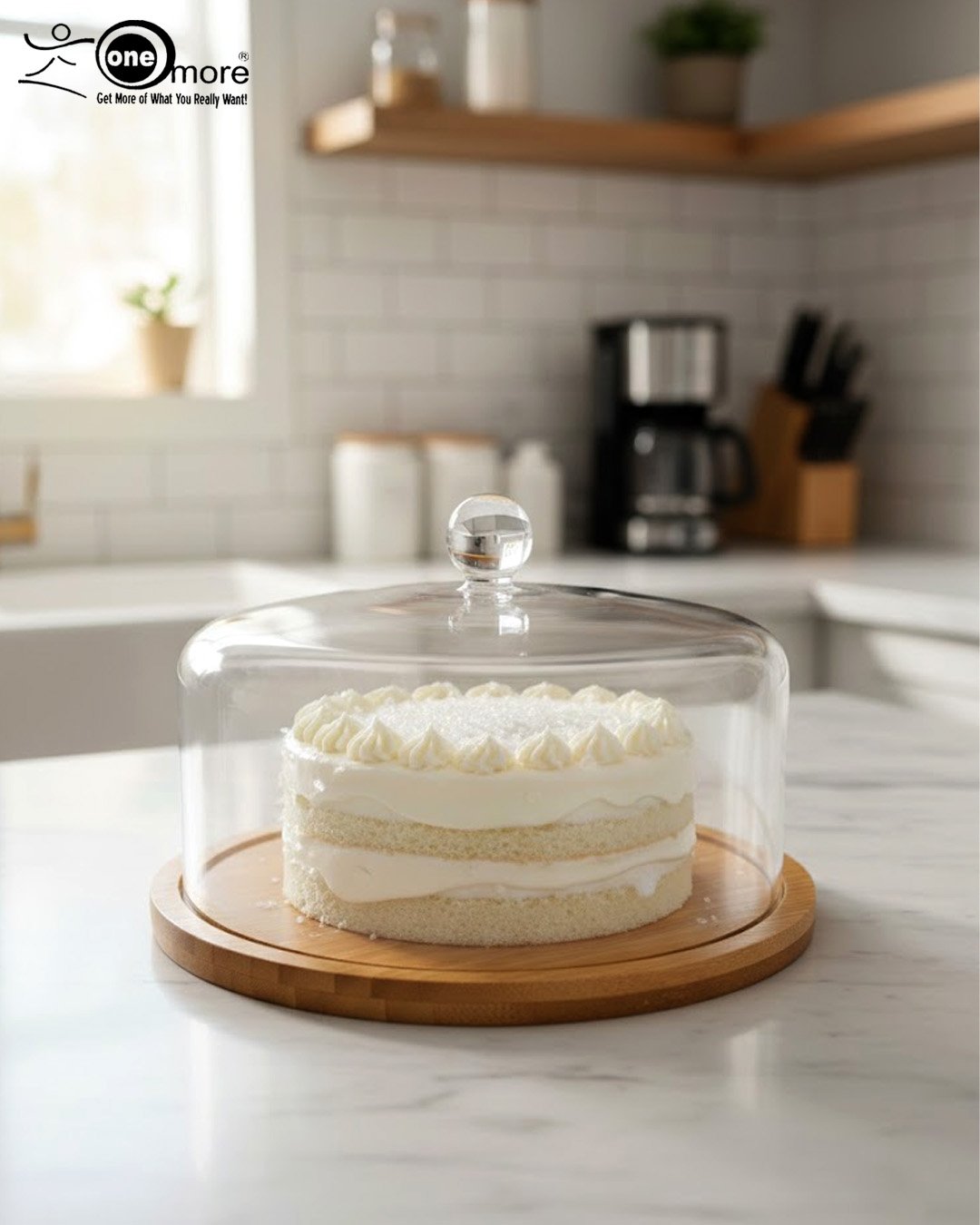 1 A white frosted layer cake displayed on a natural wooden bamboo base, covered by a clear circular acrylic dome with a round glass-like knob on a white marble kitchen counter.