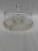 A versatile 2-in-1 clear acrylic serving set shown in two views: one as a divided platter filled with dates, raisins, and walnuts under a dome lid, and the other as a pedestal stand holding a layered chocolate cake on a marble kitchen counter.