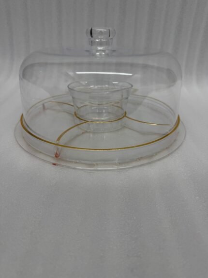 A versatile 2-in-1 clear acrylic serving set shown in two views: one as a divided platter filled with dates, raisins, and walnuts under a dome lid, and the other as a pedestal stand holding a layered chocolate cake on a marble kitchen counter.