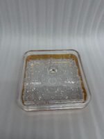 A square acrylic dry fruit dish with a gold-plated rim and crystal-patterned base, featuring a clear lid with a round knob, filled with assorted nuts and apricots on a wooden table.
