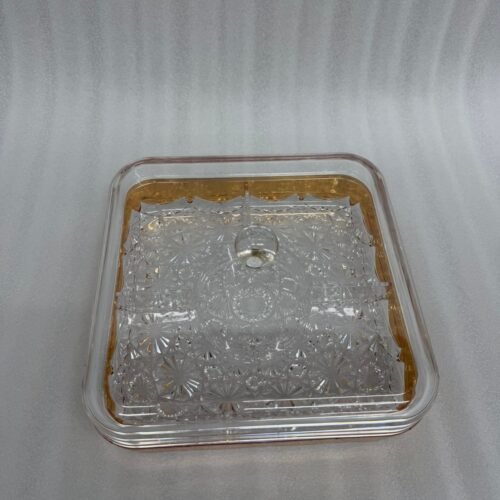 A square acrylic dry fruit dish with a gold-plated rim and crystal-patterned base, featuring a clear lid with a round knob, filled with assorted nuts and apricots on a wooden table.