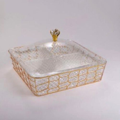 A luxury 4-compartment clear acrylic dry fruit box with a gold honeycomb pattern, filled with assorted nuts and dried apricots, displayed on a dark wooden coffee table in a modern living room.