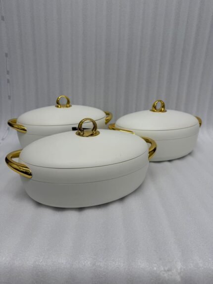 A set of three modern, oval-shaped insulated hotpots with gold handles and knobs, shown in chocolate brown, grey, and white colors on wooden and marble dining surfaces.