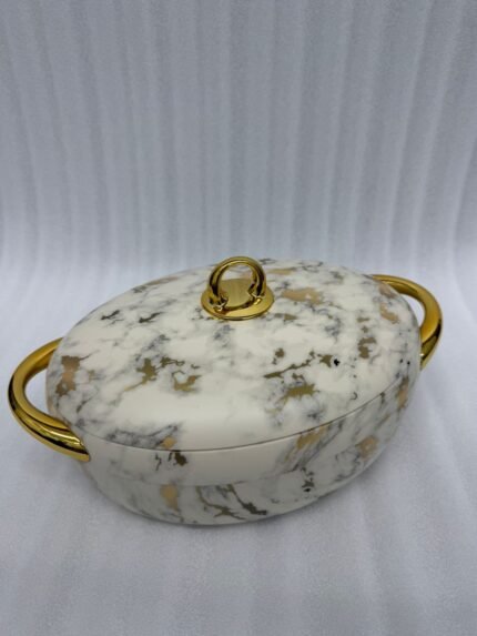 A set of three luxury marble-patterned insulated hotpots with gold handles and knobs, arranged on a wooden dining table with small bowls of condiments and a blurred restaurant BG.