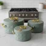 A set of three round, quilted insulated hotpots in varying sizes (1L, 2.5L, and 4L) with gold handles and lid accents, displayed on a kitchen counter and wooden dining table.