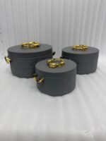 A set of three round, quilted insulated hotpots in varying sizes (1L, 2.5L, and 4L) with gold handles and lid accents, displayed on a kitchen counter and wooden dining table.