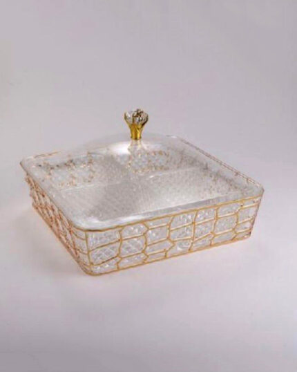 A square 4-compartment clear acrylic dry fruit box featuring a golden geometric lattice exterior and a transparent lid with a crystal knob, filled with assorted nuts and dried fruits on a wooden table.