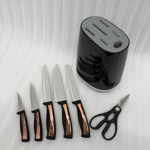 A 7-piece OneMore kitchen knife set featuring stainless steel blades and ergonomic black handles with rose gold accents, displayed both inside and next to a modern black ribbed knife block on a white marble countertop.