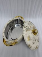 A set of three luxury marble-patterned insulated hotpots with gold handles and knobs, arranged on a wooden dining table with small bowls of condiments and a blurred restaurant BG.