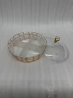 A round, transparent acrylic dry fruit server with four compartments filled with dates, apricots, almonds, and pistachios, sitting on a dark wood side table in a warmly lit living room.