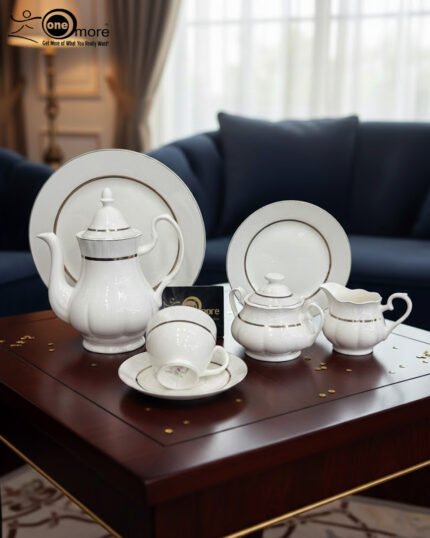 A 24-piece elegant white porcelain tea set with gold-rimmed detailing, including a teapot, sugar bowl, milk pitcher, cups, saucers, and plates, displayed on a wooden table in a luxury living room setting.