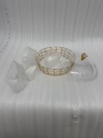 A round, transparent acrylic dry fruit server with four compartments filled with dates, apricots, almonds, and pistachios, sitting on a dark wood side table in a warmly lit living room.