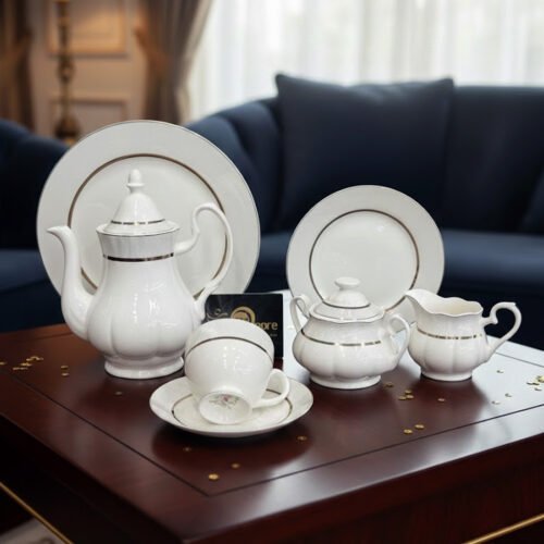 A 24-piece elegant white porcelain tea set with gold-rimmed detailing, including a teapot, sugar bowl, milk pitcher, cups, saucers, and plates, displayed on a wooden table in a luxury living room setting.
