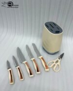 A 6-piece kitchen knife set featuring cream-colored ergonomic handles with rose gold accents, displayed both inside a matching compact storage block on a granite countertop and laid out on a white surface to show the different stainless steel blades and kitchen shears.