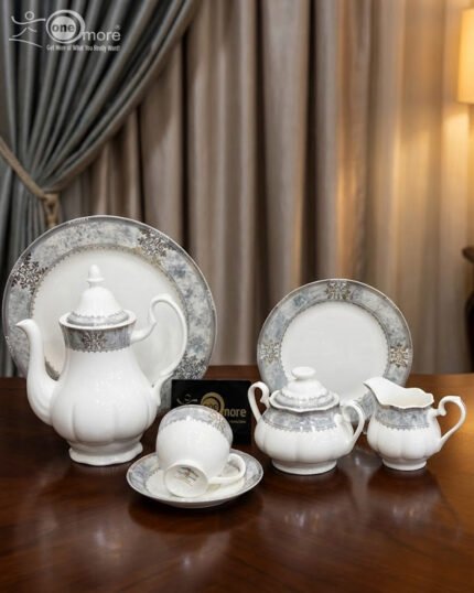 A luxury 24-piece white porcelain tea set featuring a grey marble effect border and intricate silver filigree patterns, displayed on a wooden surface against elegant neutral curtains.