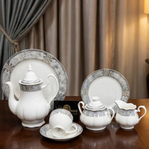 A luxury 24-piece white porcelain tea set featuring a grey marble effect border and intricate silver filigree patterns, displayed on a wooden surface against elegant neutral curtains.