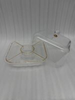 A versatile clear acrylic 2-in-1 serving dish shown in two uses: one as a divided tray filled with assorted dry fruits, nuts, and apricots, and the other as a pedestal cake stand holding a caramel-drizzled cake under a protective dome.