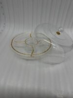 A versatile 2-in-1 clear acrylic serving dish shown in two settings: first as a pedestal cake stand holding a red velvet cake in a bright kitchen, and second as a flat sectional tray filled with almonds, pistachios, and dried apricots on a wooden coffee table.