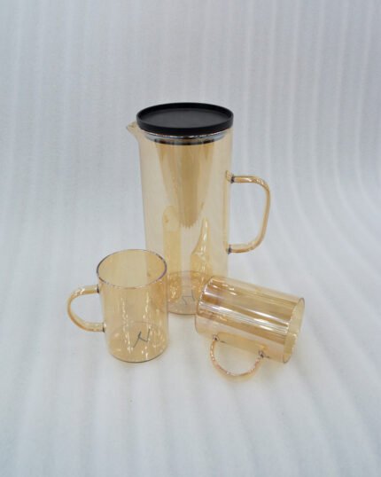 A high-quality amber-tinted glass water set featuring a tall cylindrical pitcher with a black lid and six matching glass mugs with handles, arranged on a rustic wooden table with soft natural lighting.