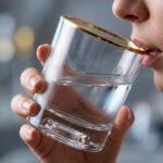 Close-up of a person drinking from a luxury RCR-inspired crystal glass with a gold-plated rim and heavy base, showcasing elegant tableware.