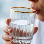 A close-up of a person holding a premium RCR-inspired crystal glass with a luxury gold rim and intricate geometric cut patterns.