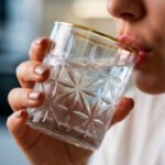 Close-up of a hand holding an RCR-inspired crystal water glass with a geometric starburst pattern and a decorative gold rim.