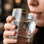 Close-up of a person holding a square-shaped crystal glass with a gold-painted rim, filled with clear water, showcasing the elegant transparency and luxury design.