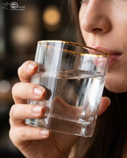 Close-up of a person holding a square-shaped crystal glass with a gold-painted rim, filled with clear water, showcasing the elegant transparency and luxury design.