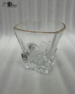 A close-up of a premium RCR-inspired crystal whiskey glass with a textured ice-like geometric base and a thin golden outline on the rim, being used to drink water.
