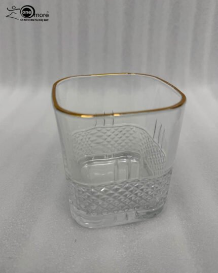 A close-up of a luxury crystal whiskey glass with a textured diamond-cut base and a thin golden rim, held by a person taking a drink.