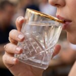 Close-up of a person drinking from a luxurious RCR-inspired crystal glass featuring an intricate diamond-cut pattern and a polished golden rim.