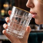 Close-up of a person drinking from a textured RCR-inspired crystal water glass with a luxurious gold rim and geometric square pattern.